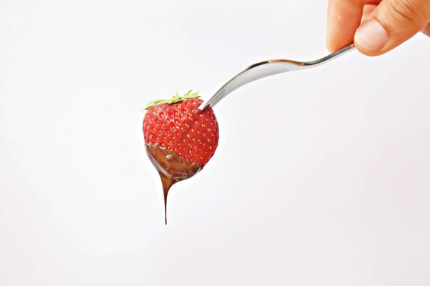 Fragole fresche, attaccate sulla punta di una forchetta, immergerle nel cioccolato liquido da vicino e isolate
 - Foto, immagini