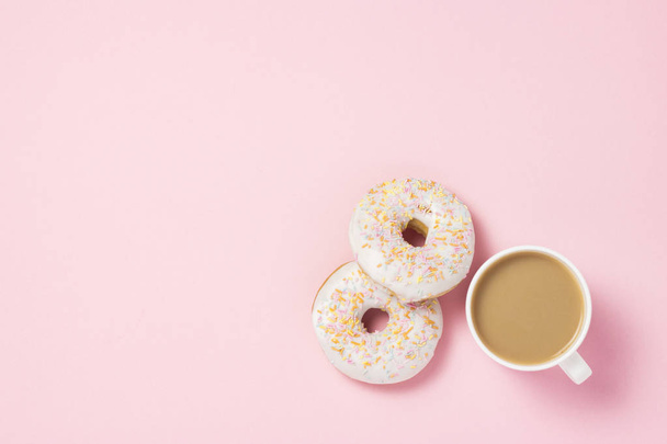 White Cup, coffee or tea with milk and fresh tasty sweet donuts on a pink background. Bakery concept, fresh pastries, delicious breakfast, fast food. Flat lay, top view - 写真・画像