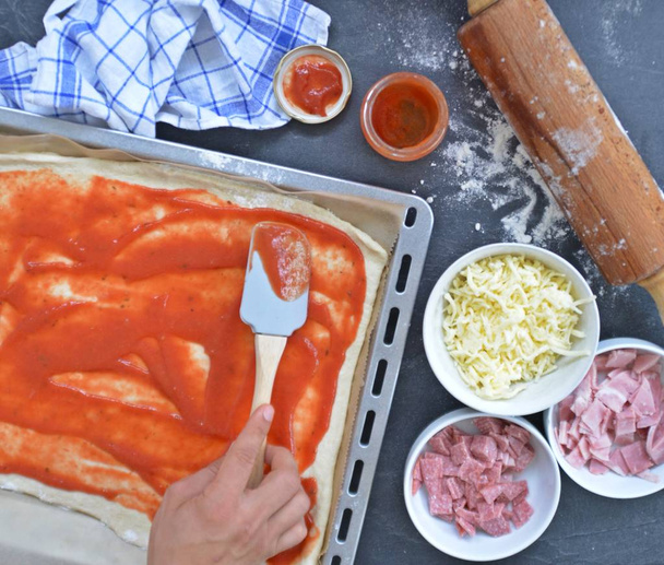 Yakın çekim-Man, jambon, salam ve peynir pişirme levha yanında malzemeler ile pizza hamur dolu bir pizza dolduruyor  - Fotoğraf, Görsel