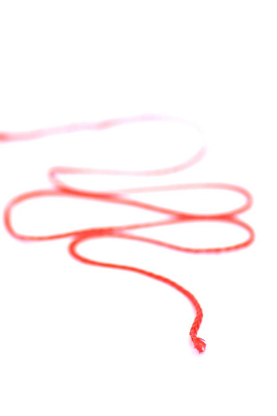 La frase alemana "el hilo de una historia" abstractamente representada como una imagen con un hilo rojo delante de un fondo blanco representa la consistencia interna de una historia
 - Foto, Imagen