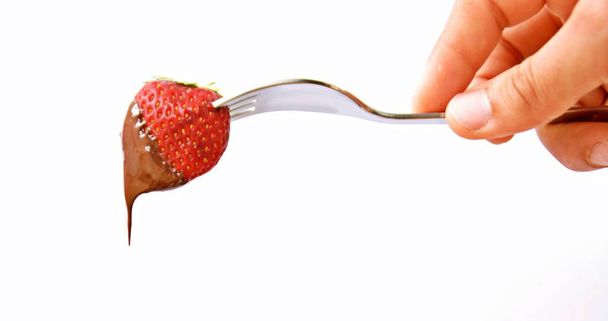 Fresh strawberries, stuck on the tip of a fork, dip in liquid chocolate - close up and isolated - Fotó, kép