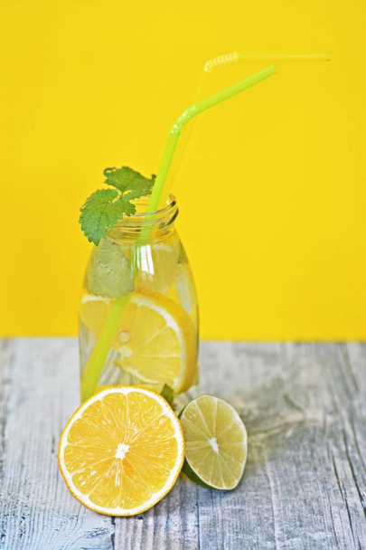 Holding a glass full of ice, limes, lemons and mint in your hand - a perfect match for the soul on a colorful background with space for text or other elements  - Photo, Image