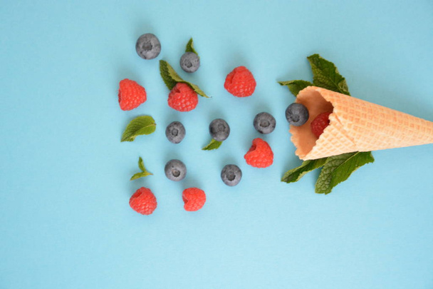 An ice cream cone with blueberries, raspberries and mint on a colorful background as a symbol of a refreshing summer fruity ice cream - Photo, image