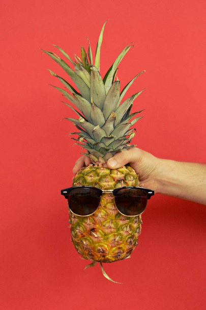 держа ананас с солнцезащитными очками в руке
 - Фото, изображение