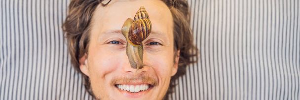 Young man makes a face mask with snail mucus. Snail crawling on a face mask. SPA for man, SPA for all BANNER, LONG FORMAT - Fotoğraf, Görsel