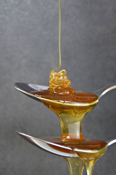 Honing stroomt over lepel op zwarte achtergrond - Foto, afbeelding