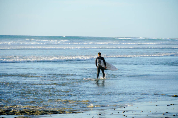 Surfer w mokrym garniturze trzymając białą deskę surfingową na plaży. La Jolla Beach, San Diego, Kalifornia,  - Zdjęcie, obraz