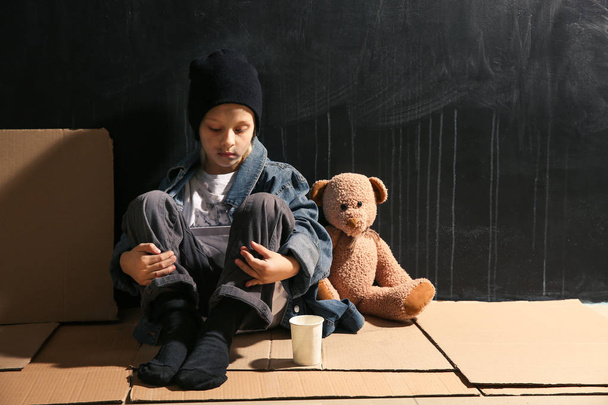 Άστεγη μικρό κορίτσι κάθεται στο πάτωμα κοντά σε σκούρο τοίχο - Φωτογραφία, εικόνα