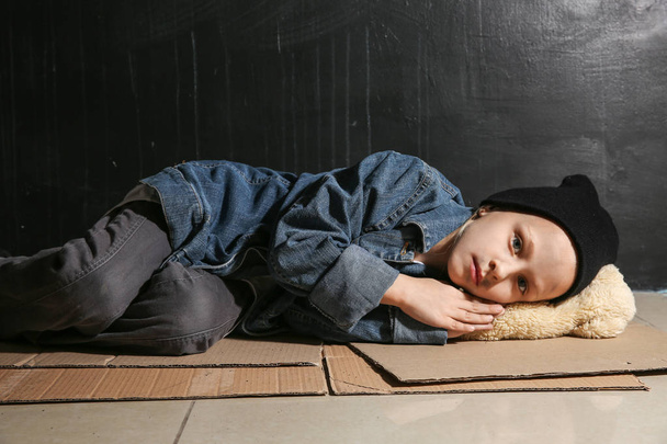 Homeless little girl lying on floor near dark wall - Photo, Image