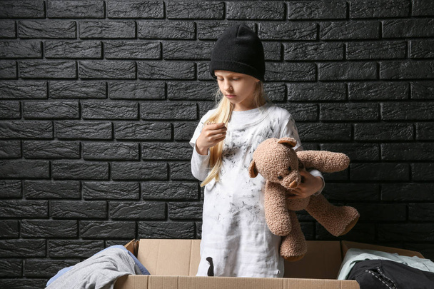 Homeless little girl with teddy bear near brick wall - 写真・画像