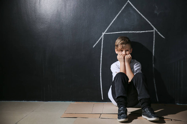 Бездомный маленький мальчик сидит на полу рядом с темной стеной
 - Фото, изображение