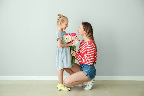 Μικρό κορίτσι χαιρετά τη μητέρα της με μπουκέτο τουλίπες στο σπίτι - Φωτογραφία, εικόνα