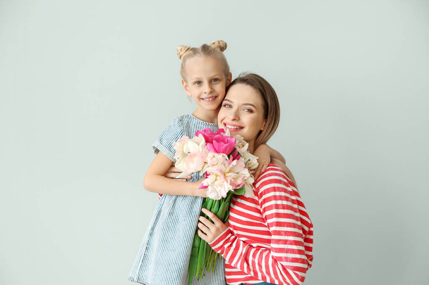 Little girl greeting her mother with bouquet of tulips on light background - Photo, Image
