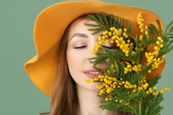 Mooie jonge vrouw met boeket van mimosa bloemen op kleur achtergrond - Foto, afbeelding