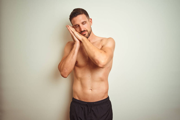 Young handsome shirtless man over isolated background sleeping tired dreaming and posing with hands together while smiling with closed eyes. - Foto, imagen