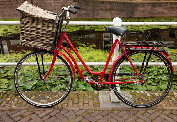Красный велосипед с корзиной припаркован у канала в Голландии
 - Фото, изображение