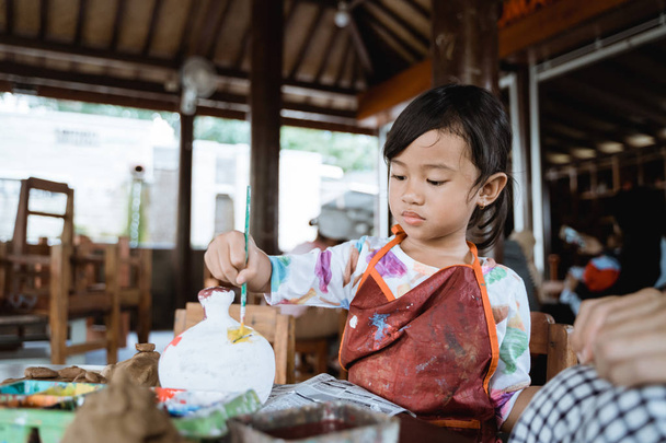 child painting ceramic pot with paint brush - Фото, зображення