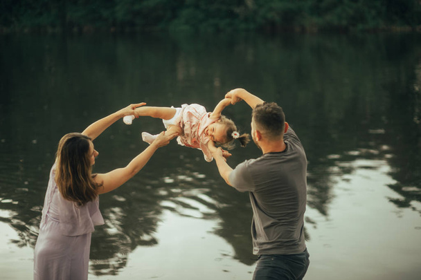 Padres felices juegan con su hija al lado del lago
. - Foto, Imagen
