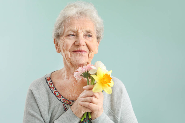 Portrait of senior woman with bouquet of flowers on grey background - Valokuva, kuva