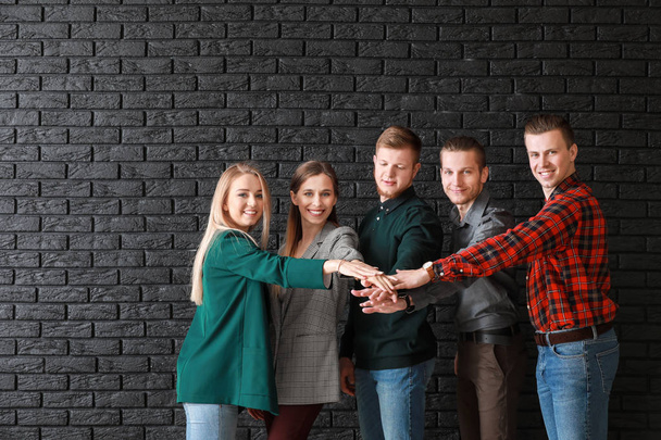 Group of young business people putting hands together on dark brick background - Photo, Image
