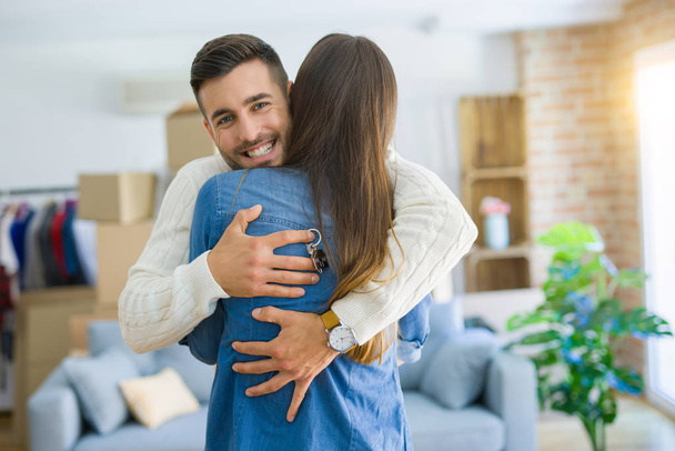 junges Paar zieht in ein neues Zuhause, umarmt sich verliebt und zeigt Schlüssel  - Foto, Bild