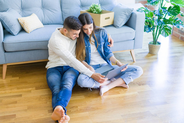 Young couple sitting on the floor of new home using computer lap - Photo, Image