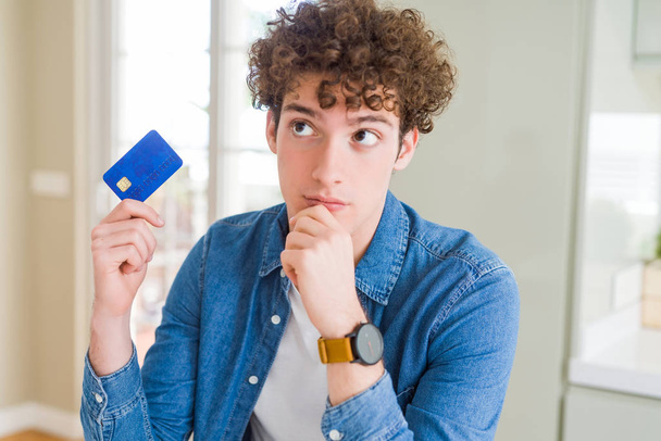 Jonge man Holding creditcard ernstige gezicht denken over vraag, zeer verward idee - Foto, afbeelding
