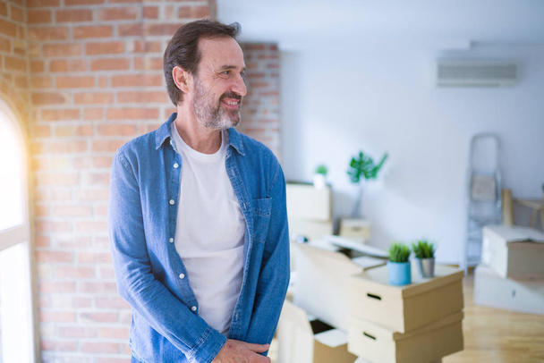 Middle age senior man moving to a new house packing cardboard boxes looking away to side with smile on face, natural expression. Laughing confident. - Photo, Image