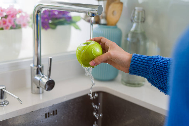 Young woman washing vegetables and fruit using water from sink - Foto, imagen