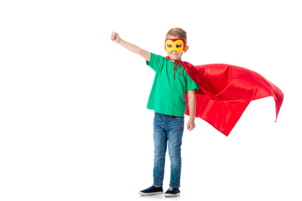 full length view of smiling preschooler boy in mask and red hero cloack standing with fist up isolated on white - Foto, immagini