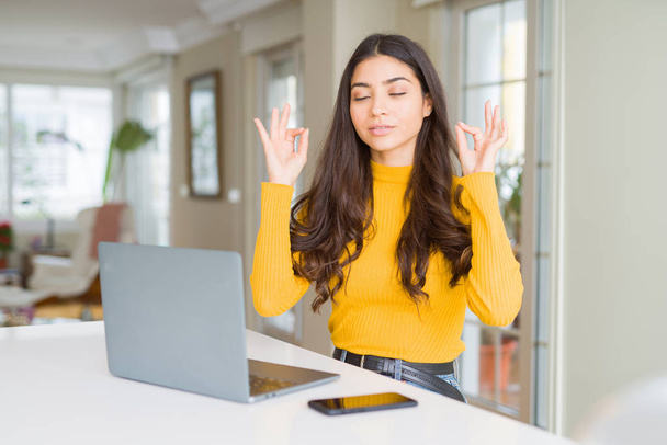 Jovem mulher usando computador portátil relaxar e sorrir com os olhos fechados fazendo gesto de meditação com os dedos. Conceito de ioga
. - Foto, Imagem