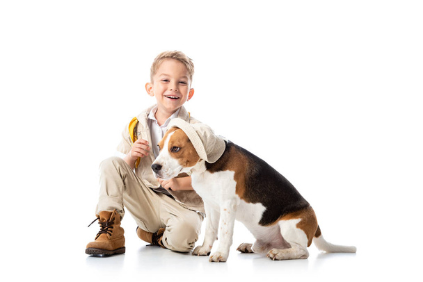 smiling preschooler explorer kid and beagle dog in hat on white - Zdjęcie, obraz
