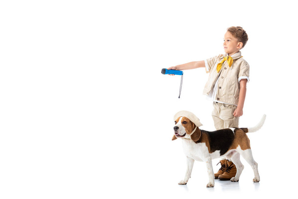 full length view of explorer child holding flashlight and beagle dog in hat on white - Photo, Image