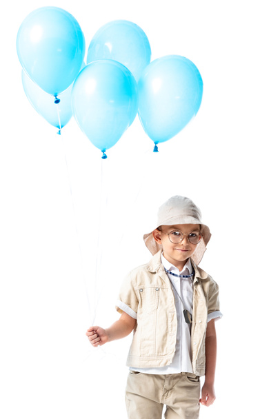 smiling explorer kid in glasses and hat holding blue balloons and looking at camera isolated on white - Foto, imagen
