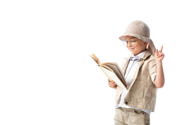 focused smiling explorer child in glasses reading book and showing idea sign isolated on white - Photo, Image