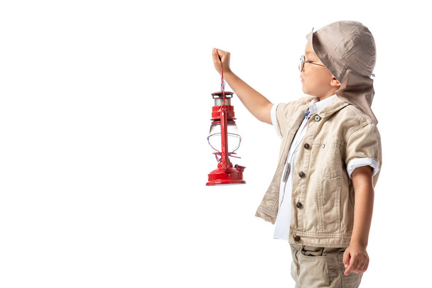 side view of explorer boy in glasses and hat holding red lantern isolated on white - Photo, Image