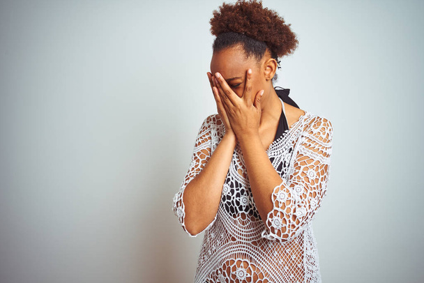 Jovem afro-americana com cabelo afro vestindo um biquíni sobre fundo branco isolado com expressão triste cobrindo o rosto com as mãos enquanto chora. Conceito de depressão
. - Foto, Imagem