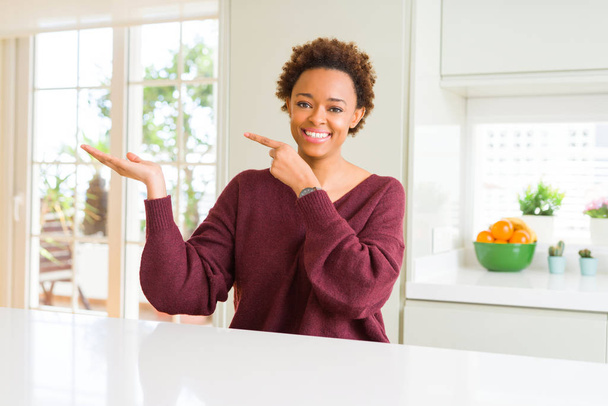 Молода жінка красива афро-американських вдома вражений і усміхнений на камеру під час представлення рукою і вказуючи пальцем. - Фото, зображення