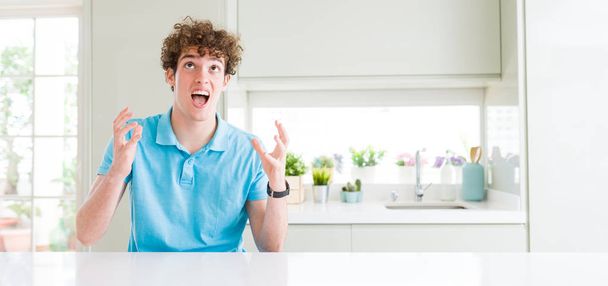 Wide shot of young handsome man at home crazy and mad shouting and yelling with aggressive expression and arms raised. Frustration concept. - Foto, Bild