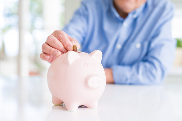 Close up of man putting a coin inside of piggy bank as savings - Photo, Image