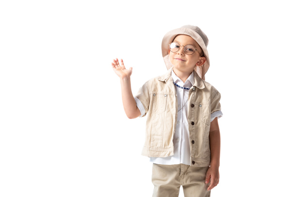 smiling explorer boy in hat and glasses looking at camera and waving hand isolated on white - Fotografie, Obrázek