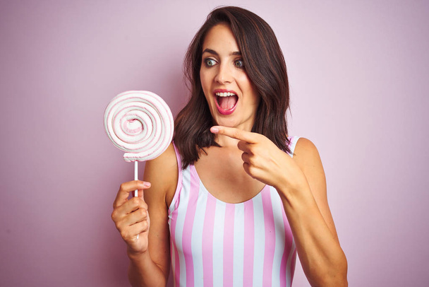 Fiatal szép nő étkezési édes édességet mint rózsaszín elszigetelt háttér nagyon boldog mutatva kéz-és ujj - Fotó, kép