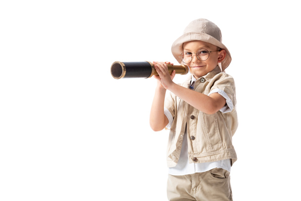 Любопытный улыбающийся исследователь мальчик в очках и шляпе, держащий шпионский стакан изолирован на белом
 - Фото, изображение