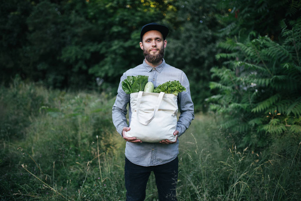 Man holding an eco bag filled with grocery. Vegetables and fruits are hanging from the bag. Ecology concept of environment protection - Photo, image