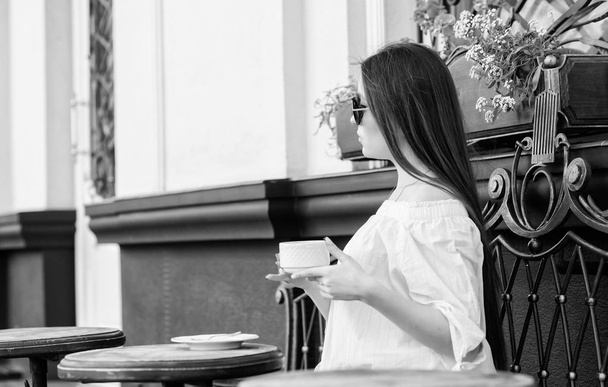 Girl enjoy morning coffee. Waiting for date. Woman in sunglasses drink coffee outdoors. Girl relax in cafe cappuccino cup. Caffeine dose. Coffee for energetic successful day. Breakfast time in cafe - Foto, Imagem