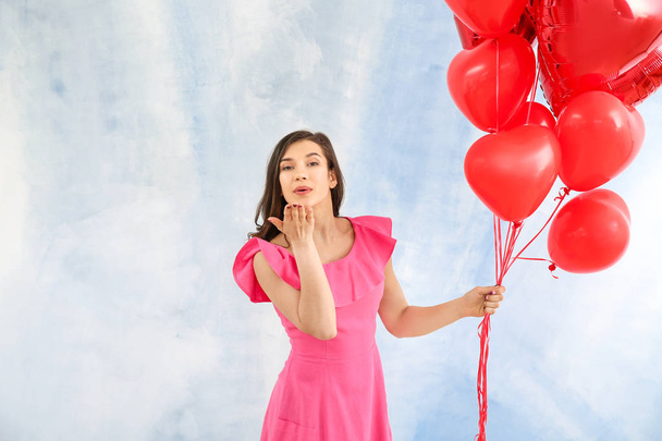 Kalp şeklinde hava balonları renkli arka planda öpücük üfleme ile güzel genç kadın - Fotoğraf, Görsel