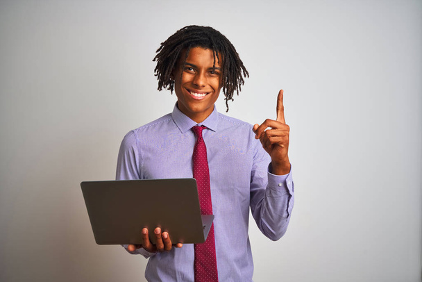 Афро-американский бизнесмен с дредами с помощью ноутбука на изолированном белом фоне удивлен идеей или вопросом указывая пальцем со счастливым лицом, номер один
 - Фото, изображение