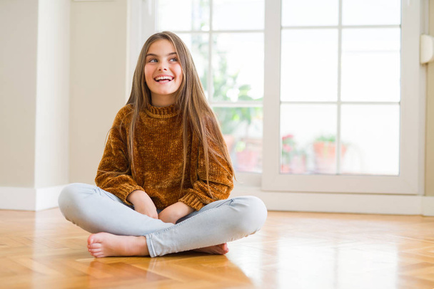 schönes junges Mädchen, das zu Hause auf dem Fußboden sitzt und mit einem Lächeln im Gesicht zur Seite schaut, natürlicher Ausdruck. Lachen selbstbewusst. - Foto, Bild
