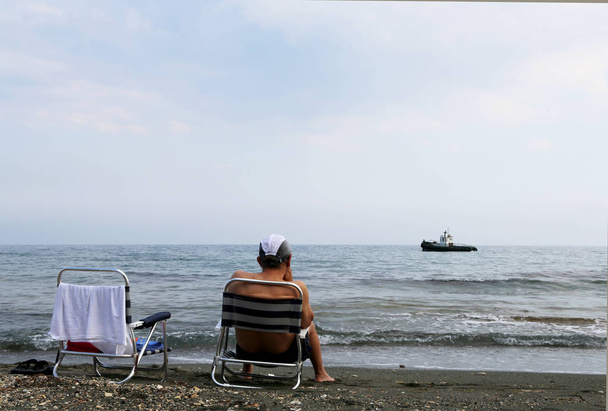 Sandalyede oturan adam denize açılan eski bir gemiyi izliyor. - Fotoğraf, Görsel