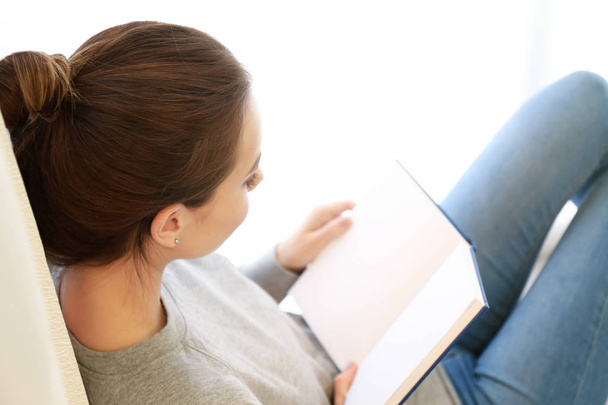 Beautiful young woman reading book at home - Фото, изображение
